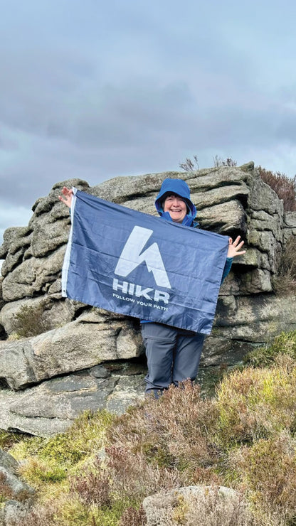 Person holding a HIKR flag on rocky terrain with a cloudy sky