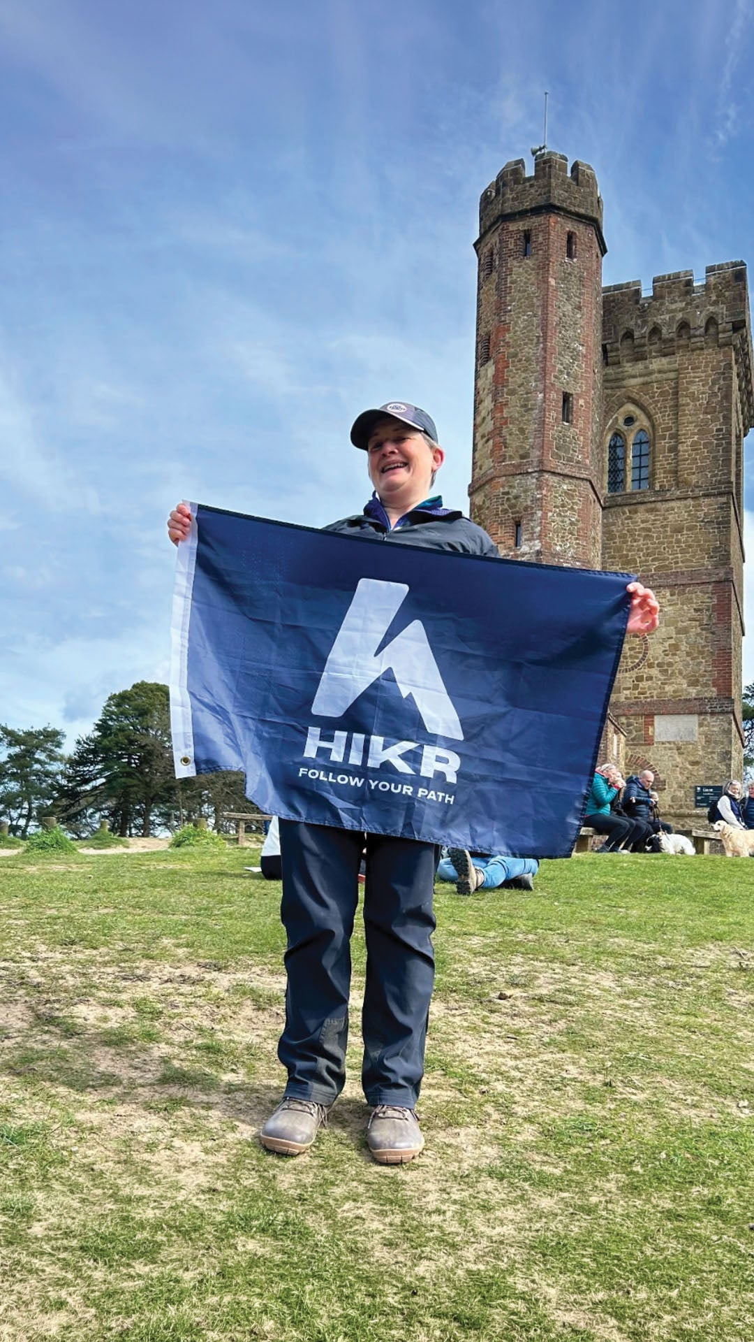 Person holding a blue HikR flag in front of a castle-like structure on a sunny day.