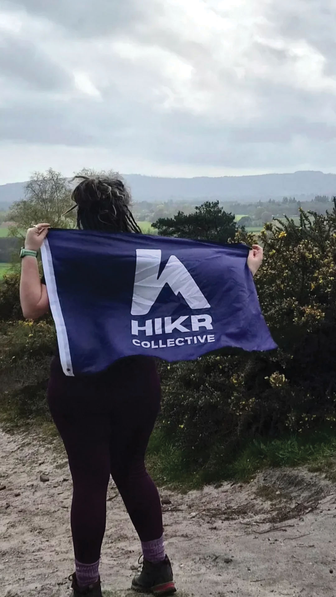 Person holding a purple flag with 'HIKR Collective' logo in a natural setting