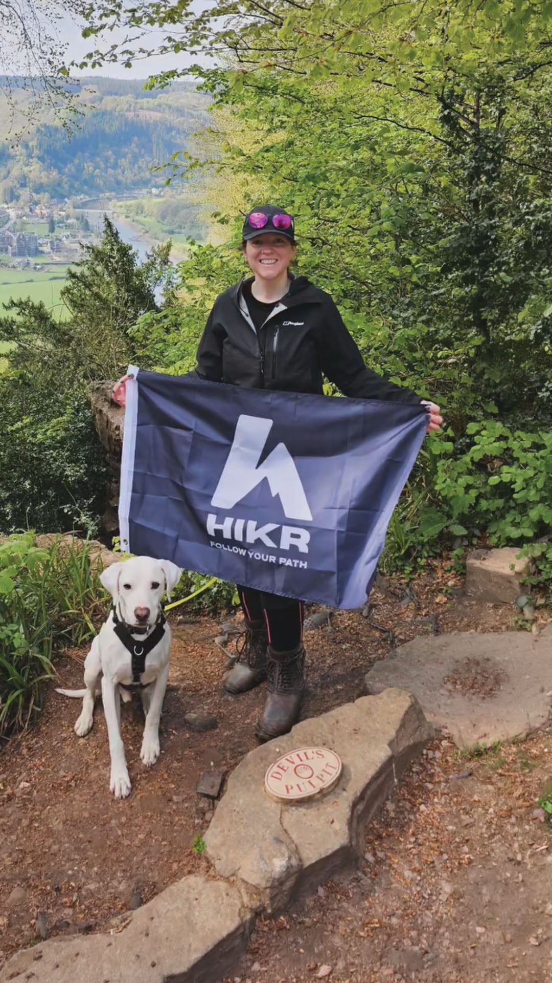Person holding a HIKR flag with a dog on a trail