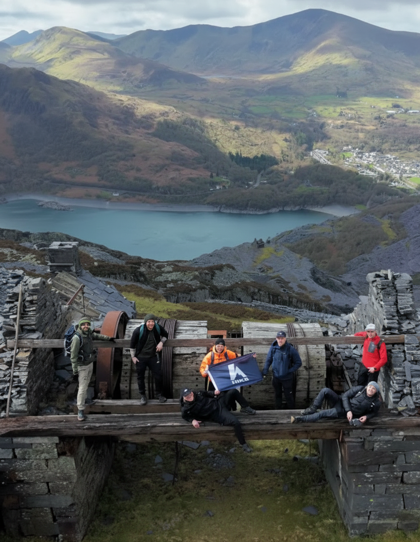 Group of people holding a HIKR Flag on a stone bridge with mountains and a lake in the background