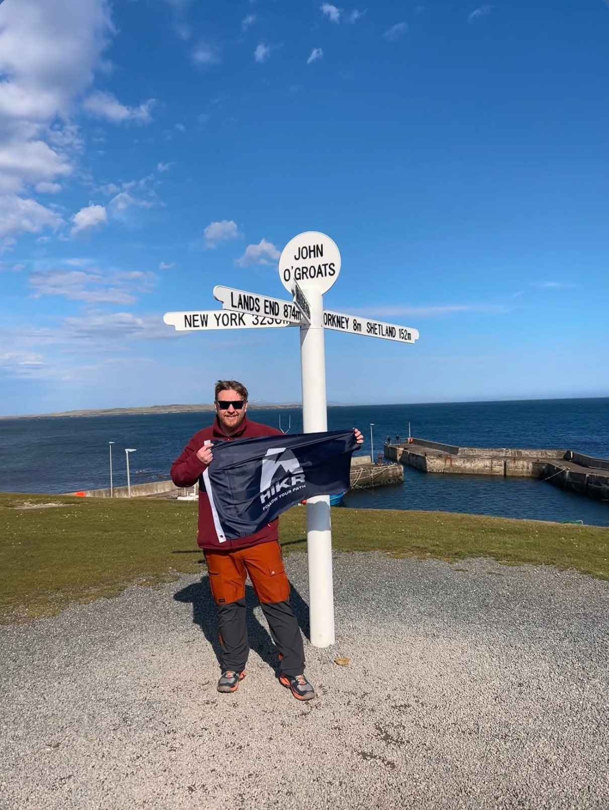 Person holding HIKR flag at a John O'Groats sign