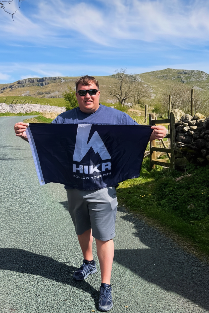 Person holding a Hikr FLAG with mountains and a dog in the background