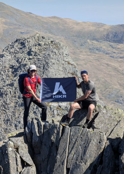 Two hikers on a mountain peak holding a HIKR Flag.