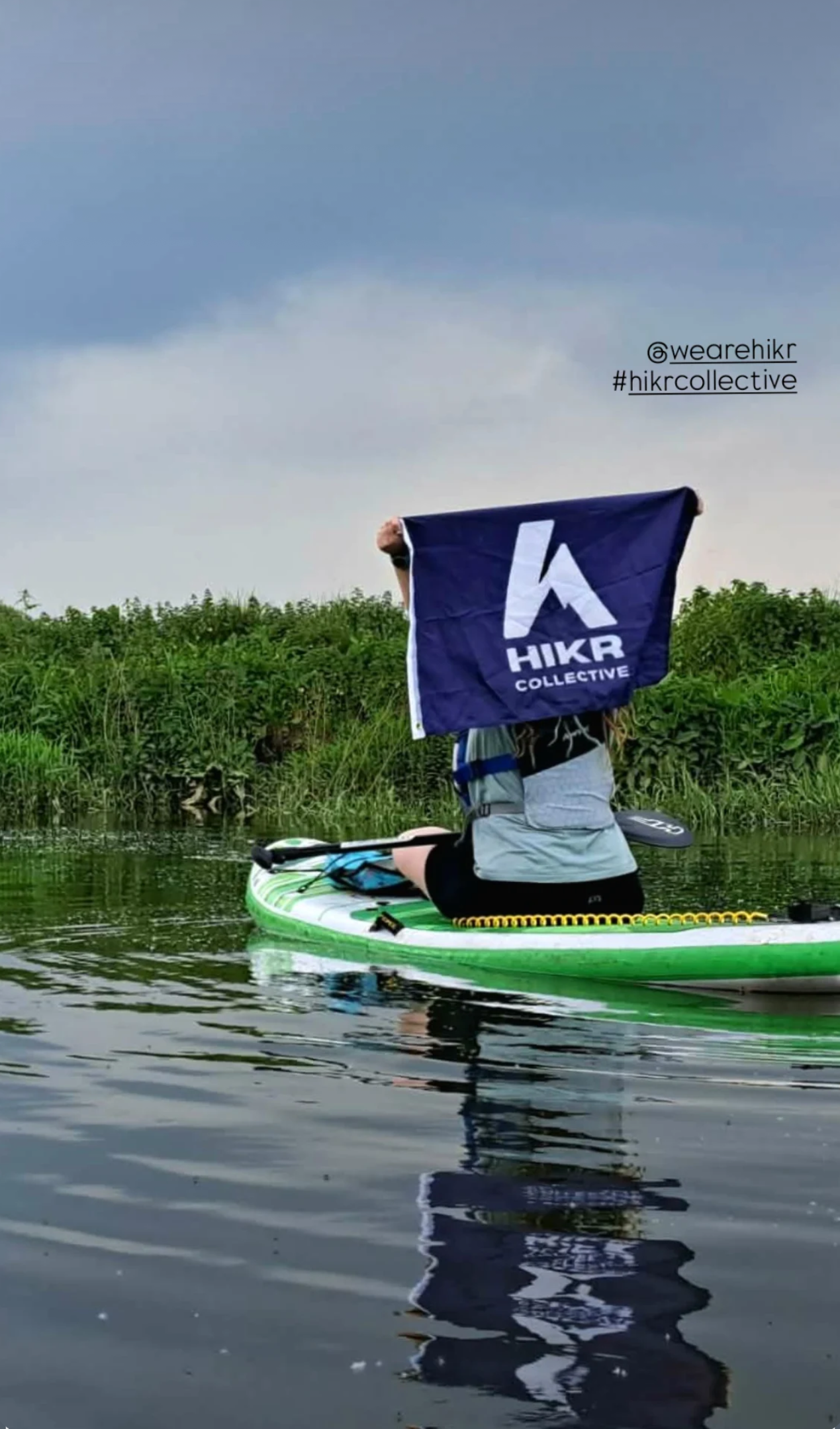 Person paddleboarding on a lake with a HikR Collective flag in the foreground