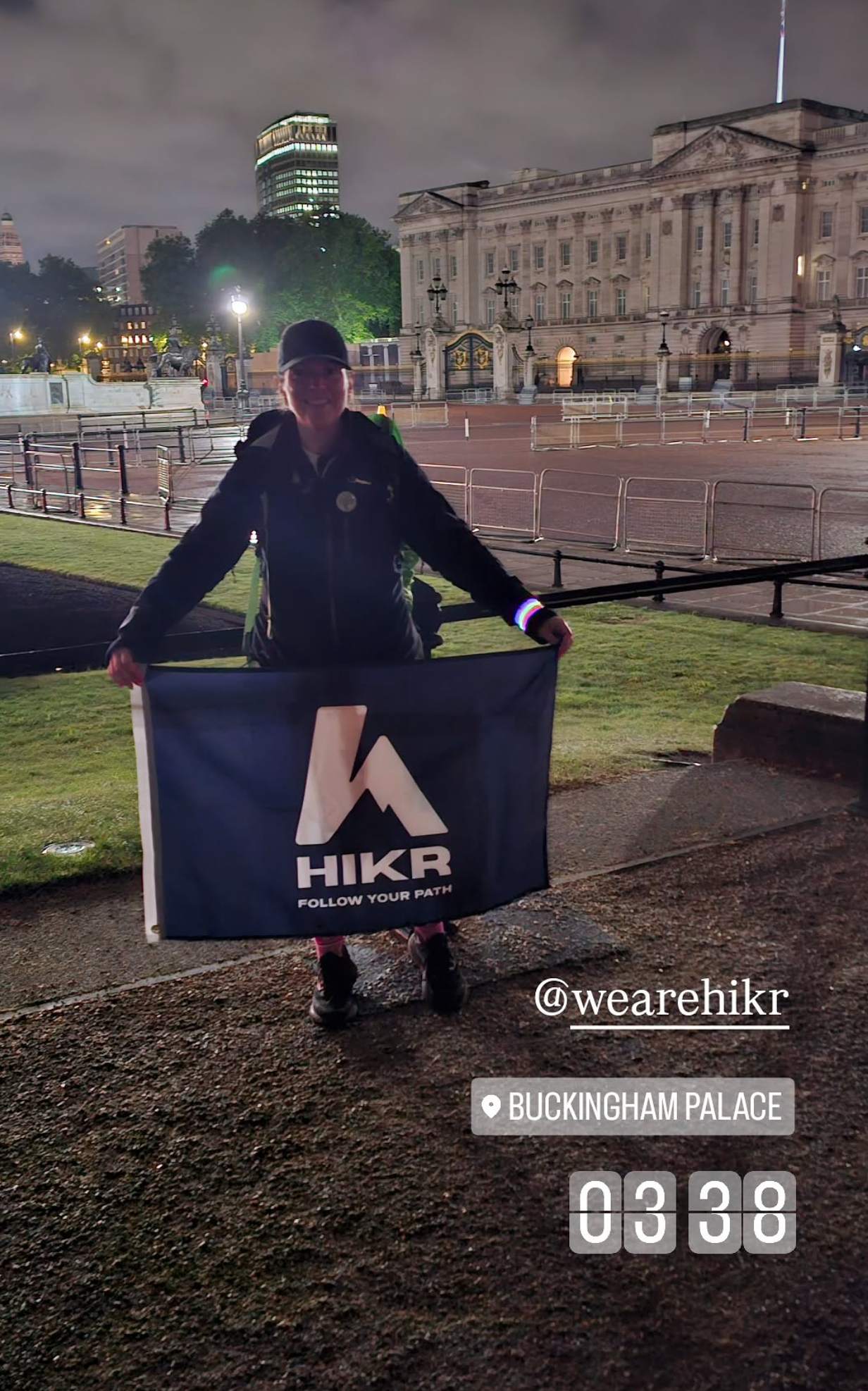 Person holding a HIKR flag in front of Buckingham Palace at night
